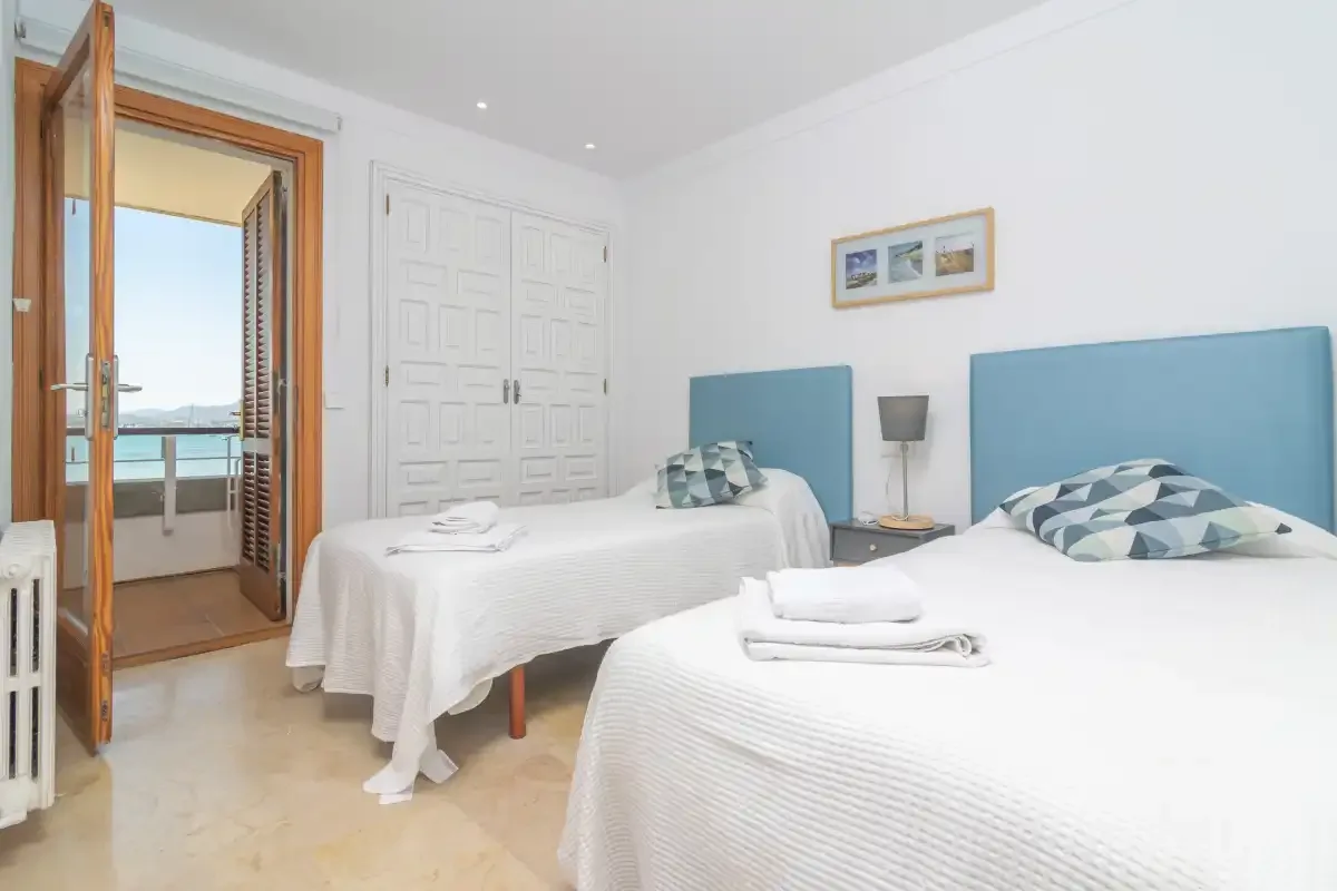 A bright bedroom with two beds and an open balcony door.