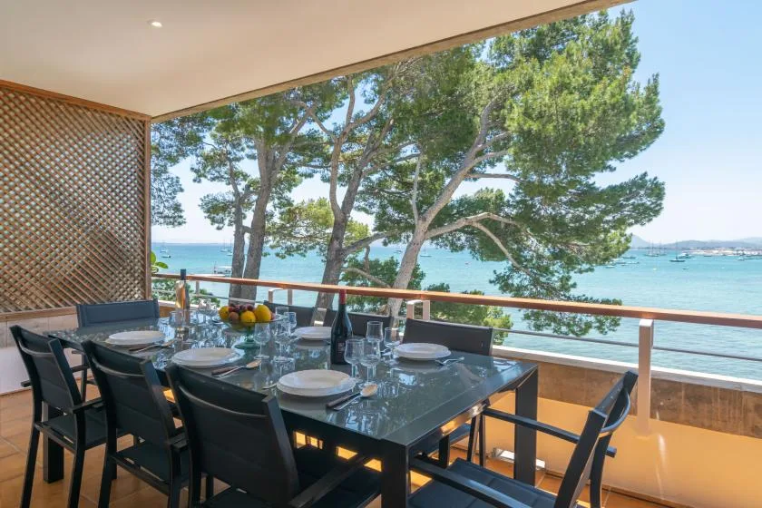 An outdoor dining area overlooks the sea, with trees along the shoreline.