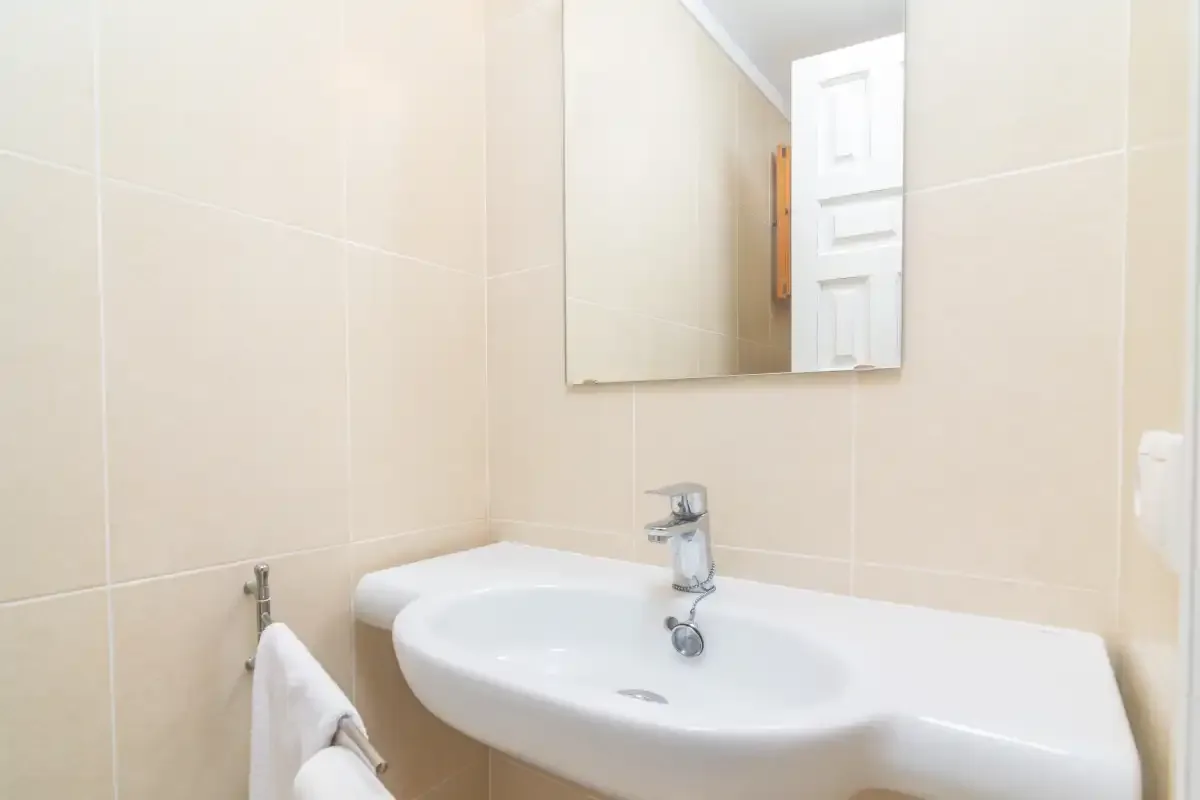 A bathroom sink and mirror are set against pale tiled walls.