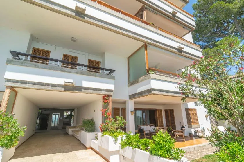 A multi-level white building with balconies, a covered driveway, and a garden.