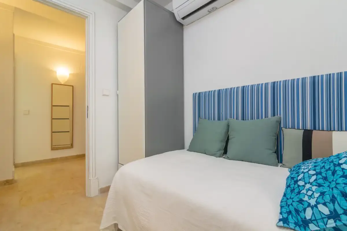 A bedroom with a bed, blue striped headboard, and doorway to a lit hall.