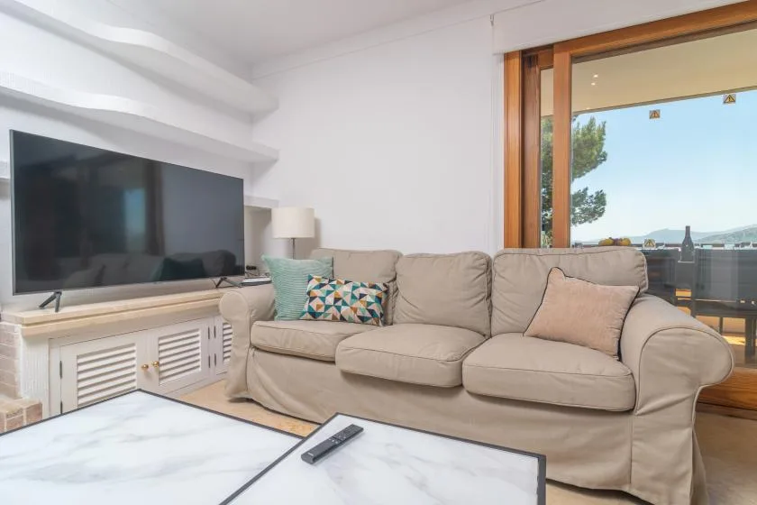 A bright living room with a beige sofa, television, and large window.