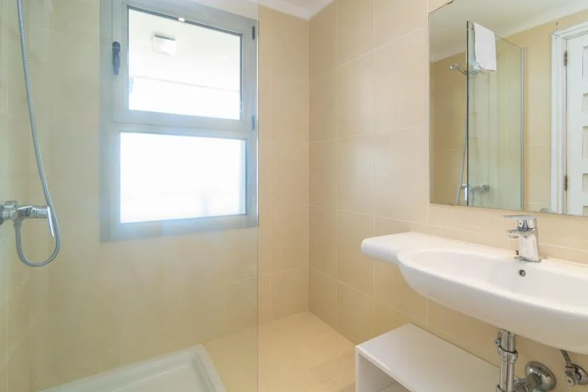 A bright bathroom with a shower, window, and sink.