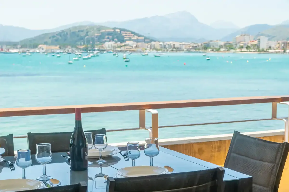 A waterfront dining table overlooks a bay dotted with boats and backed by mountains.
