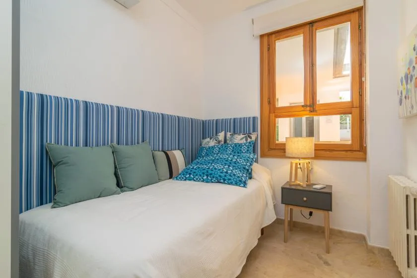 A bedroom with a neatly made bed beside a wooden-framed window.