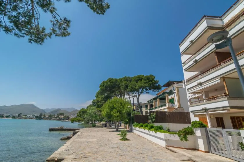 A paved waterfront promenade runs beside apartment buildings and calm blue water.