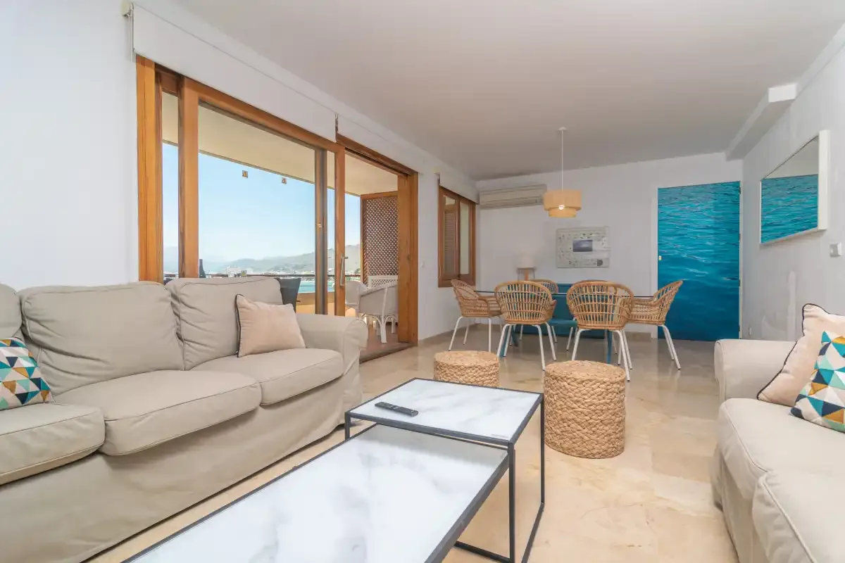 A bright living and dining area with seating, a table, and large windows.