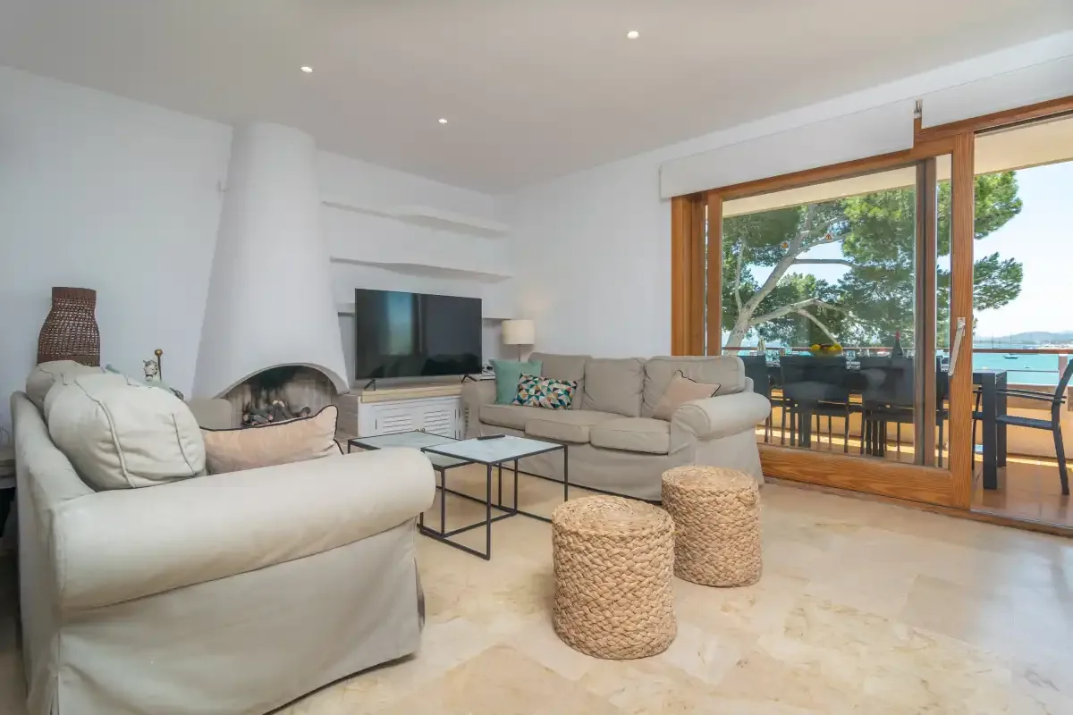 A bright living room with seating, a television, and glass doors opening onto a balcony.