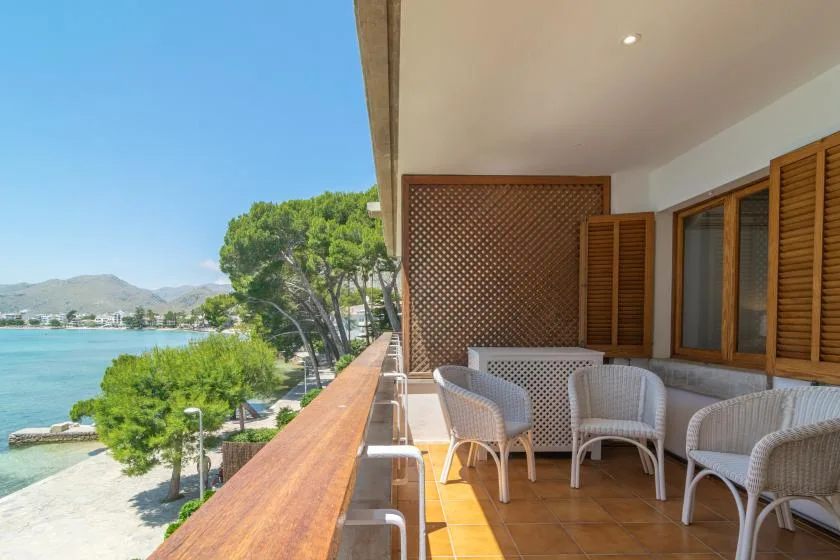 A covered balcony with wicker seating overlooks the water and distant hills.