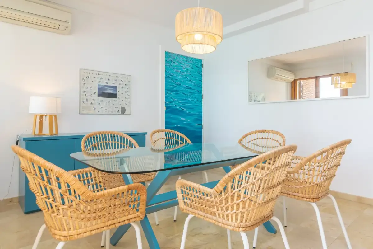 A dining area with woven seating around a glass table and blue cabinetry.