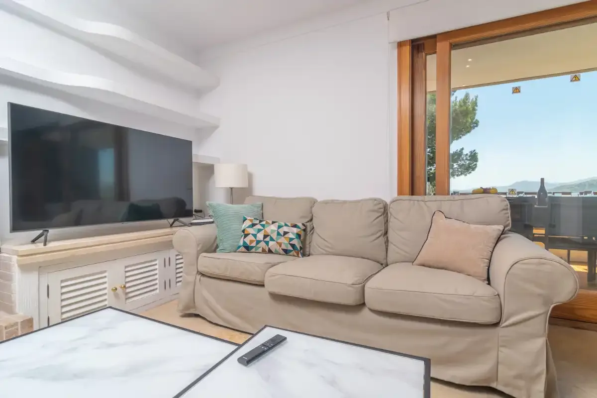 A bright living room with a beige sofa, television, and large window.