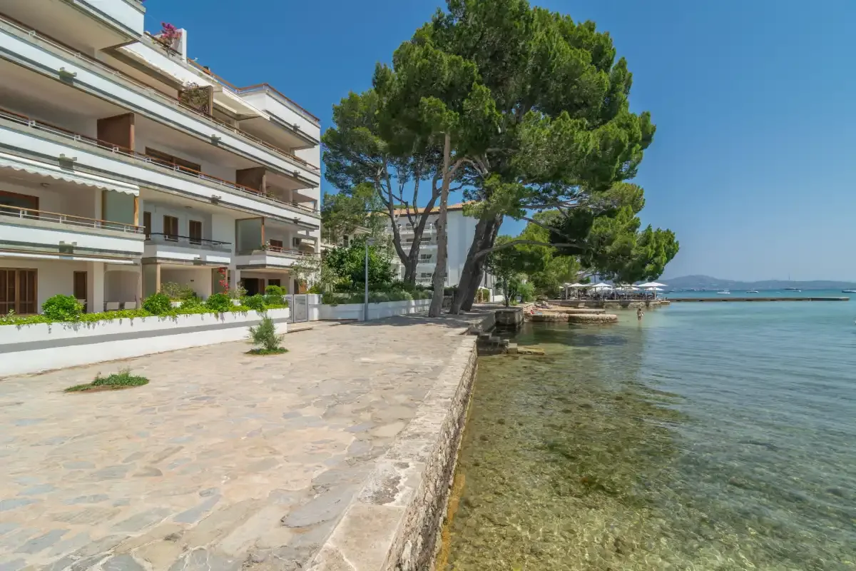 A waterfront promenade runs beside an apartment building and calm, shallow water.
