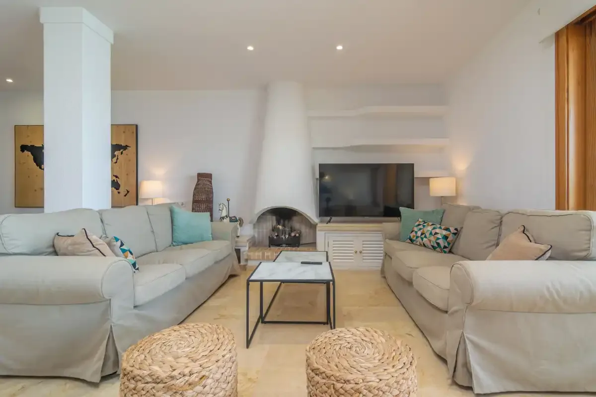 A bright living room has light seating arranged around a coffee table and television.