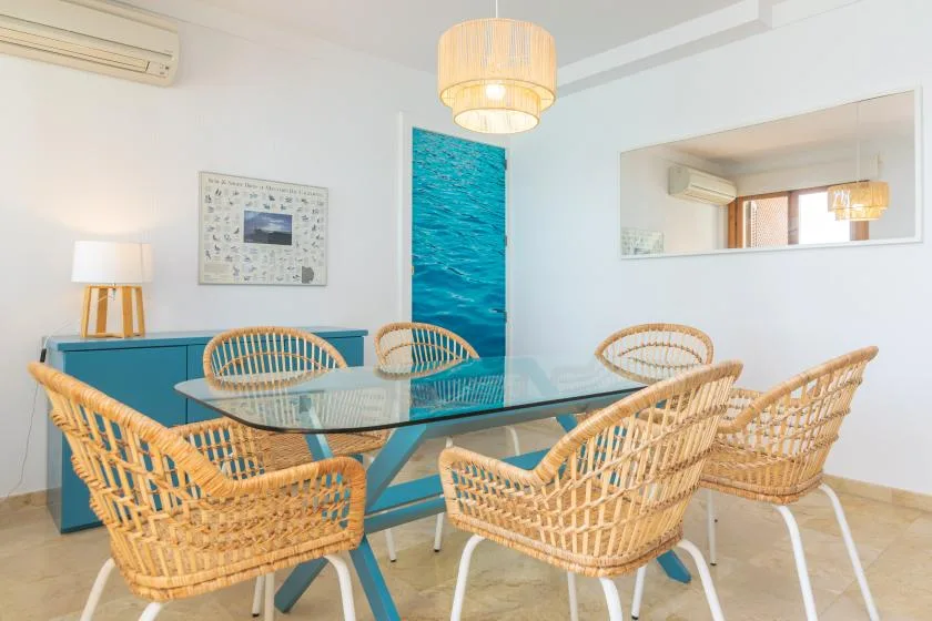 A dining area with a glass table, woven seating, and blue accents.
