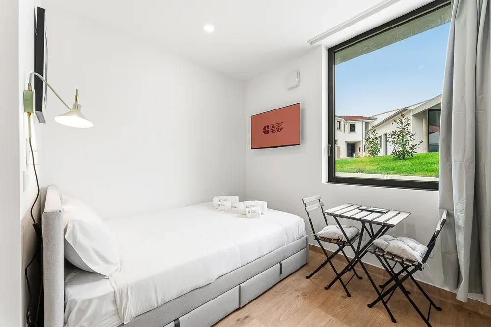 A bright bedroom with a bed and a small seating area beside the window.