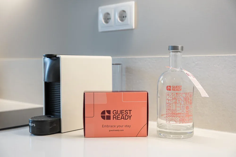 A kitchen counter displays a coffee machine, a welcome card, and a glass bottle.