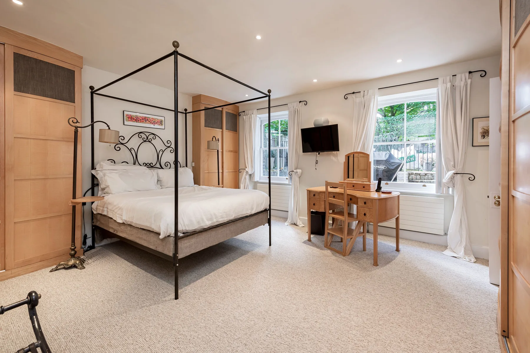 A bright bedroom with a four-poster bed and a desk by the window.