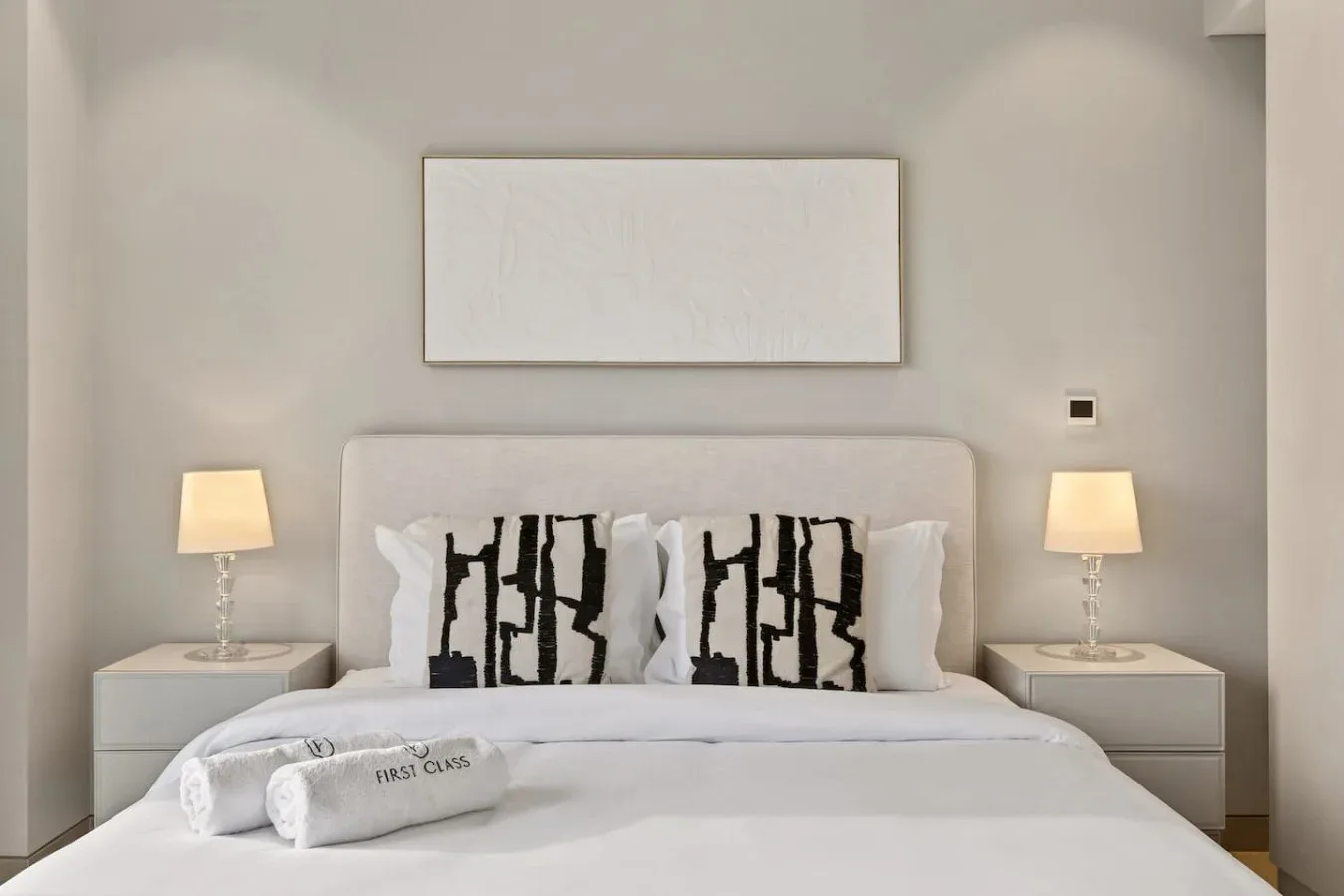 Una cama bien tendida con almohadas estampadas está bajo un cuadro sencillo.