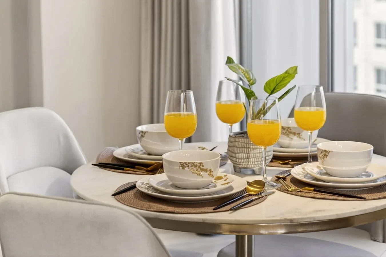 Una mesa de comedor está puesta con platos, jugo de naranja y una planta pequeña.