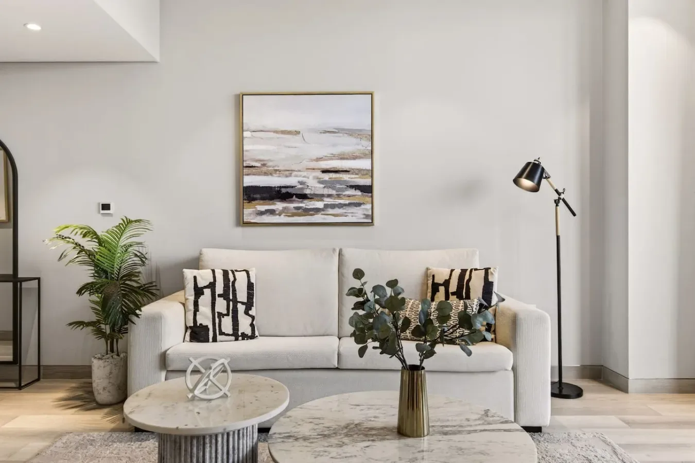 Una sala luminosa con un sofá, una obra enmarcada y una lámpara de pie.