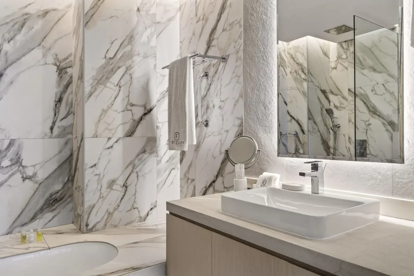 Baño con azulejos de mármol, lavabo, espejo y ducha de vidrio.