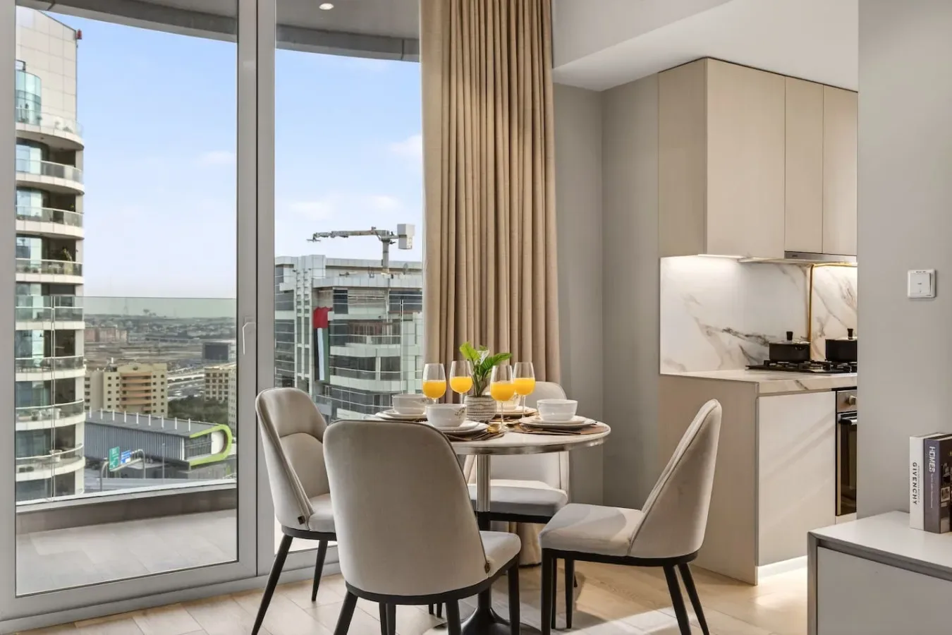 Comedor con la mesa puesta junto a ventanales que dan a edificios cercanos.
