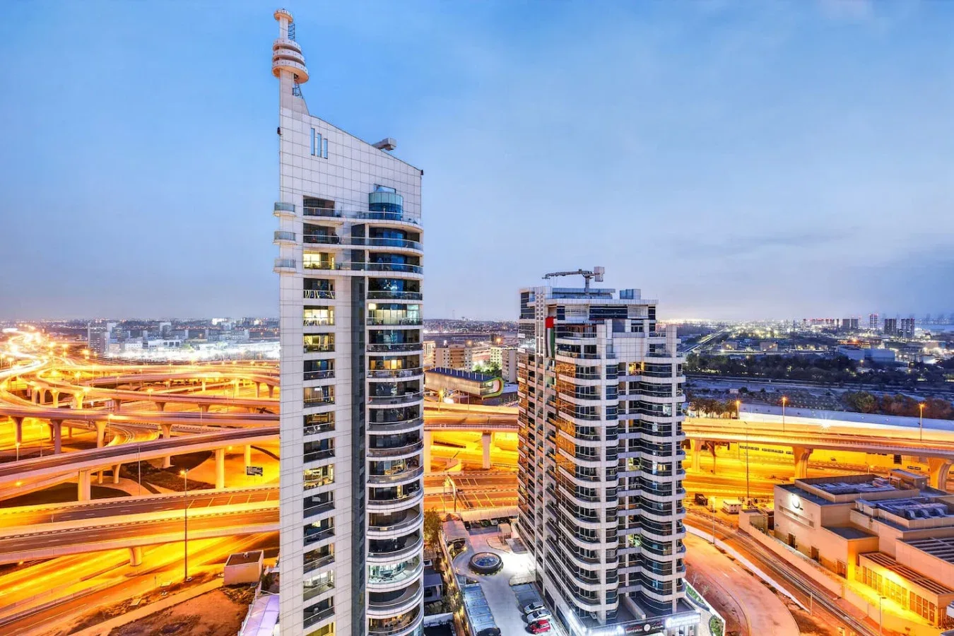 Un horizonte urbano al atardecer, con edificios altos junto a intercambiadores viales iluminados.