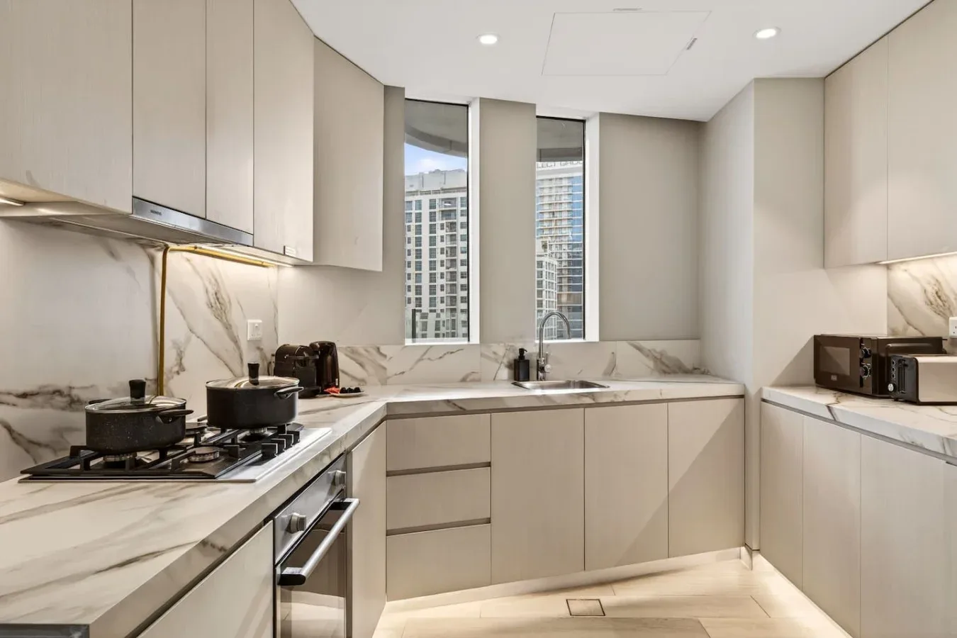 Una cocina moderna con gabinetes claros, encimeras veteadas y ventanas.