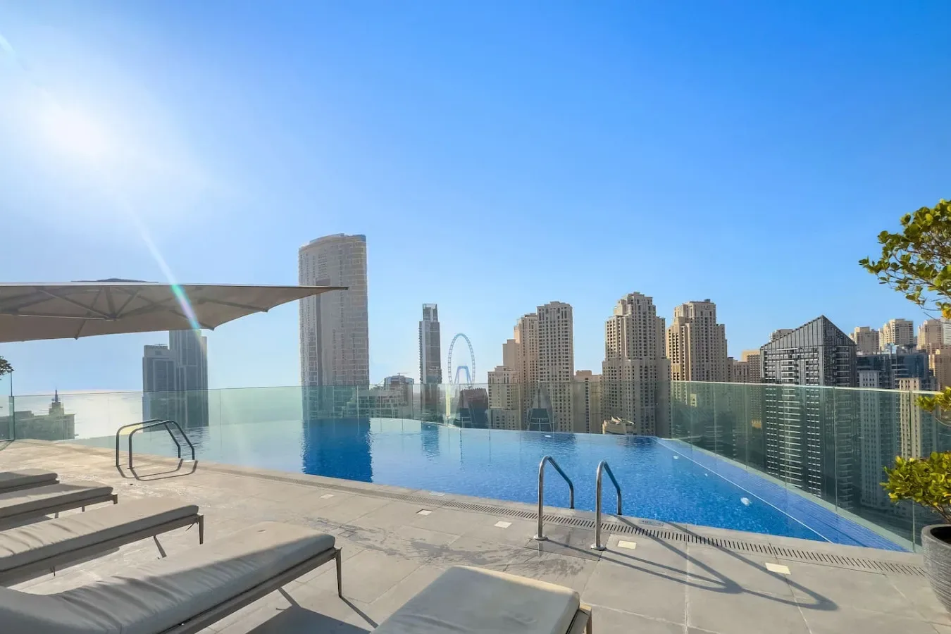 An outdoor swimming pool overlooks a city skyline, with lounge seating beside it.