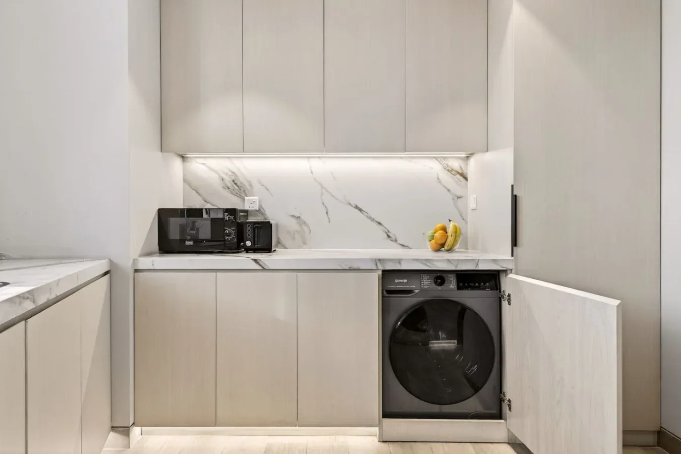 Una cocina moderna con gabinetes claros, una encimera y una lavadora de carga frontal.