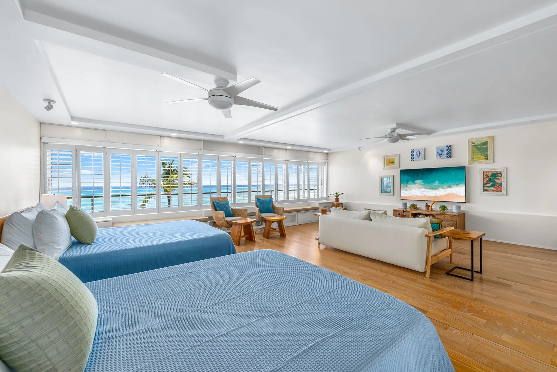 A bright bedroom and sitting area with blue bedding, seating, and wide windows.