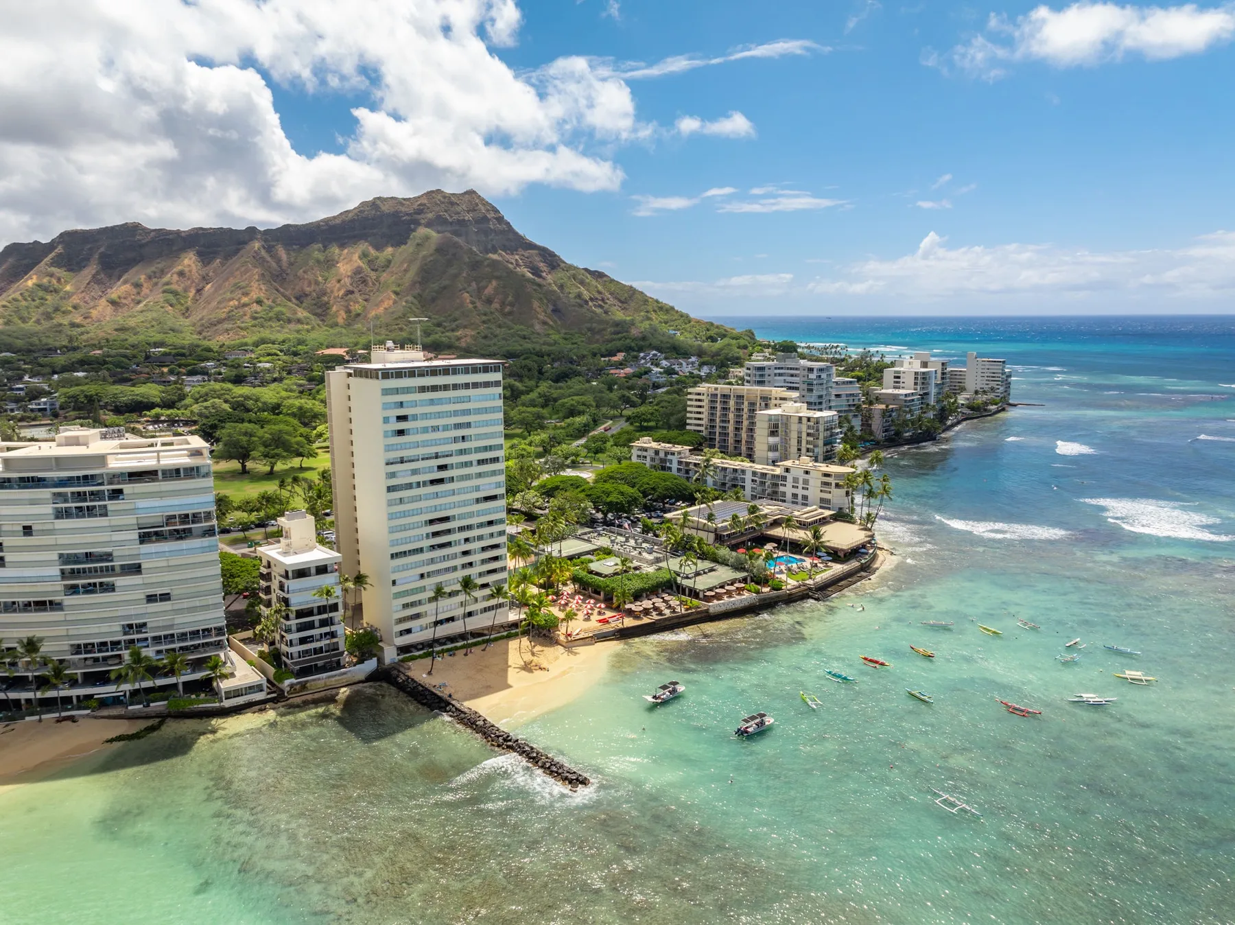 A coastal resort district with high-rise buildings along a turquoise bay beneath a mountain.