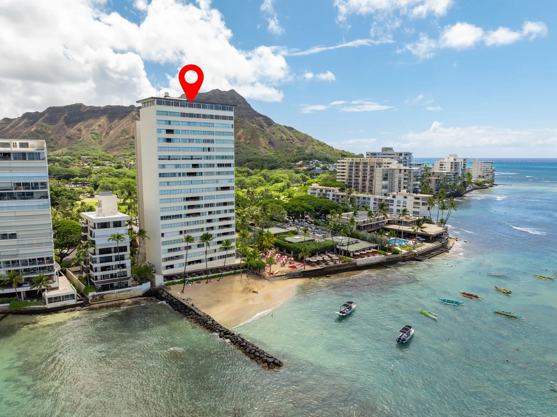 Coastal hotel buildings line a sandy beach beside clear blue water.