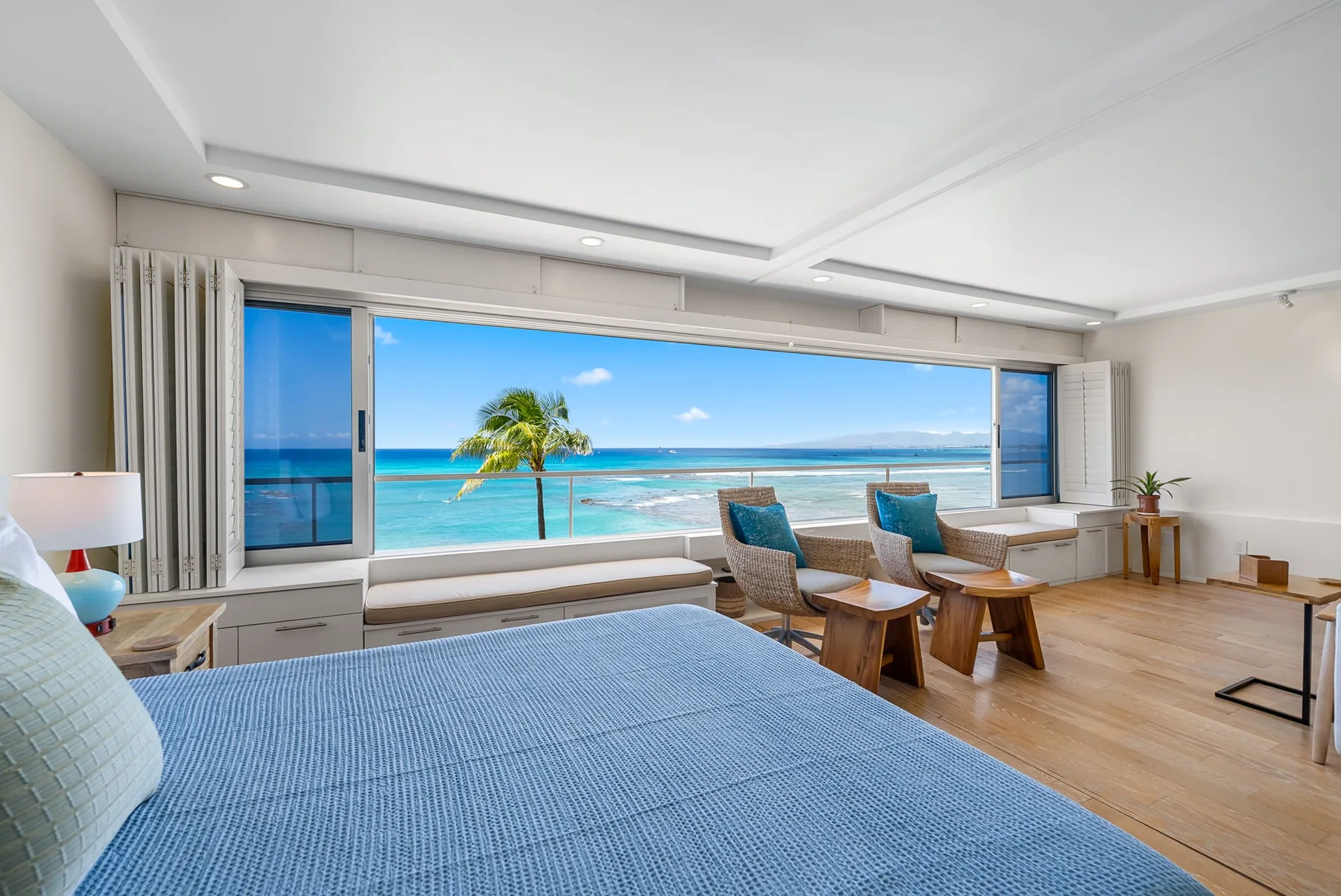 A bright bedroom with a large bed and wide windows overlooking the ocean.