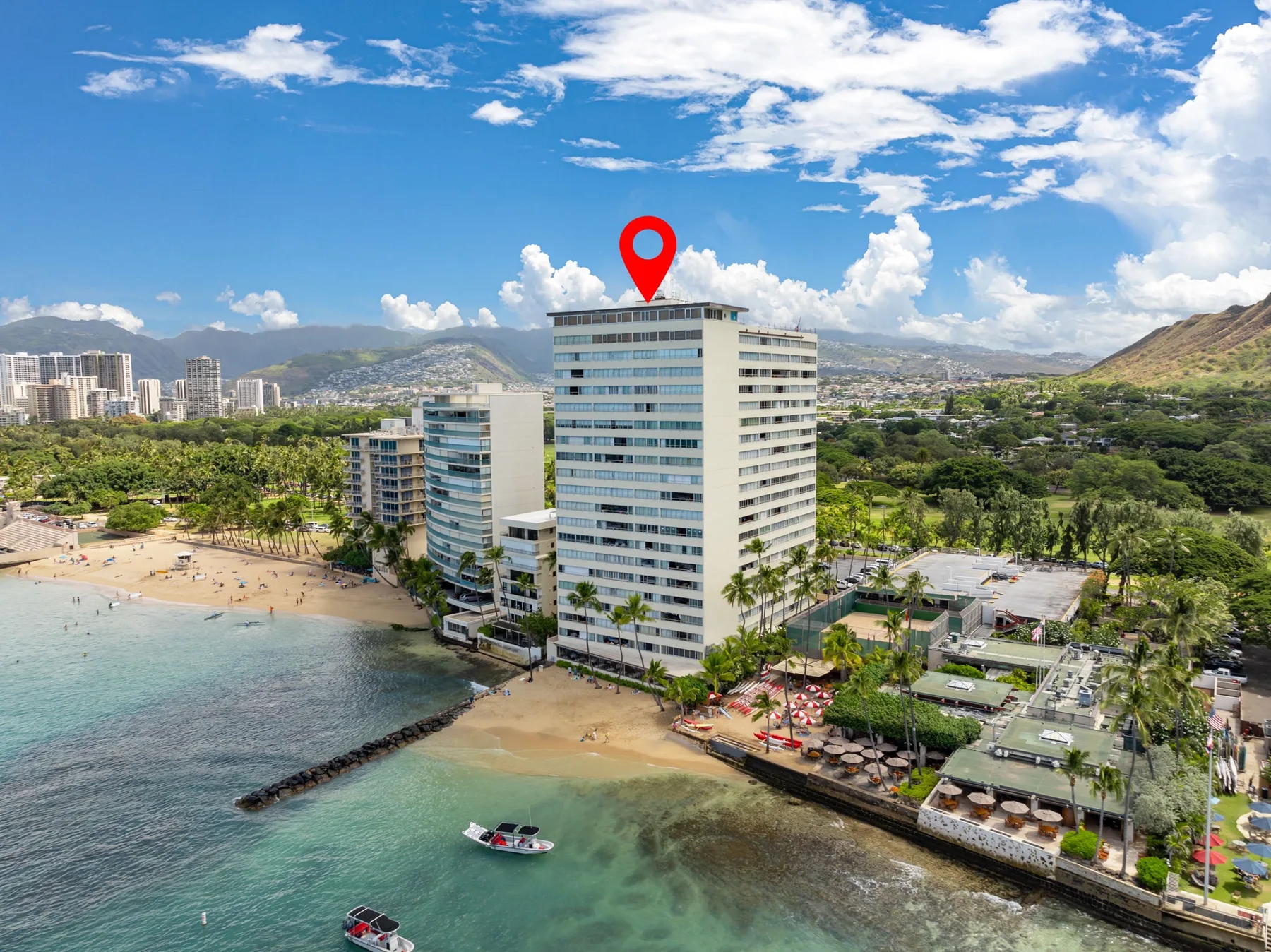 Aerial view of a tall beachfront building beside a sandy beach and turquoise water.