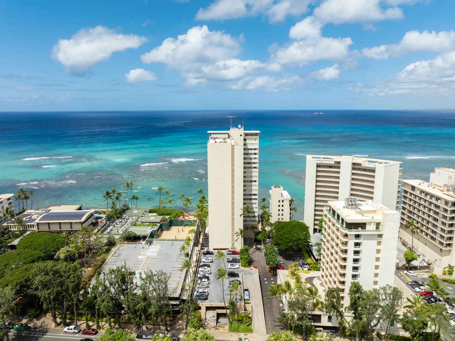 A coastal city skyline overlooks turquoise water beneath a partly cloudy sky.