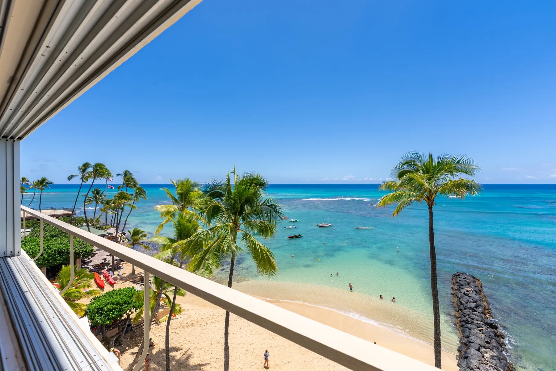 A balcony overlooks a sandy beach, palm trees, and turquoise ocean water.