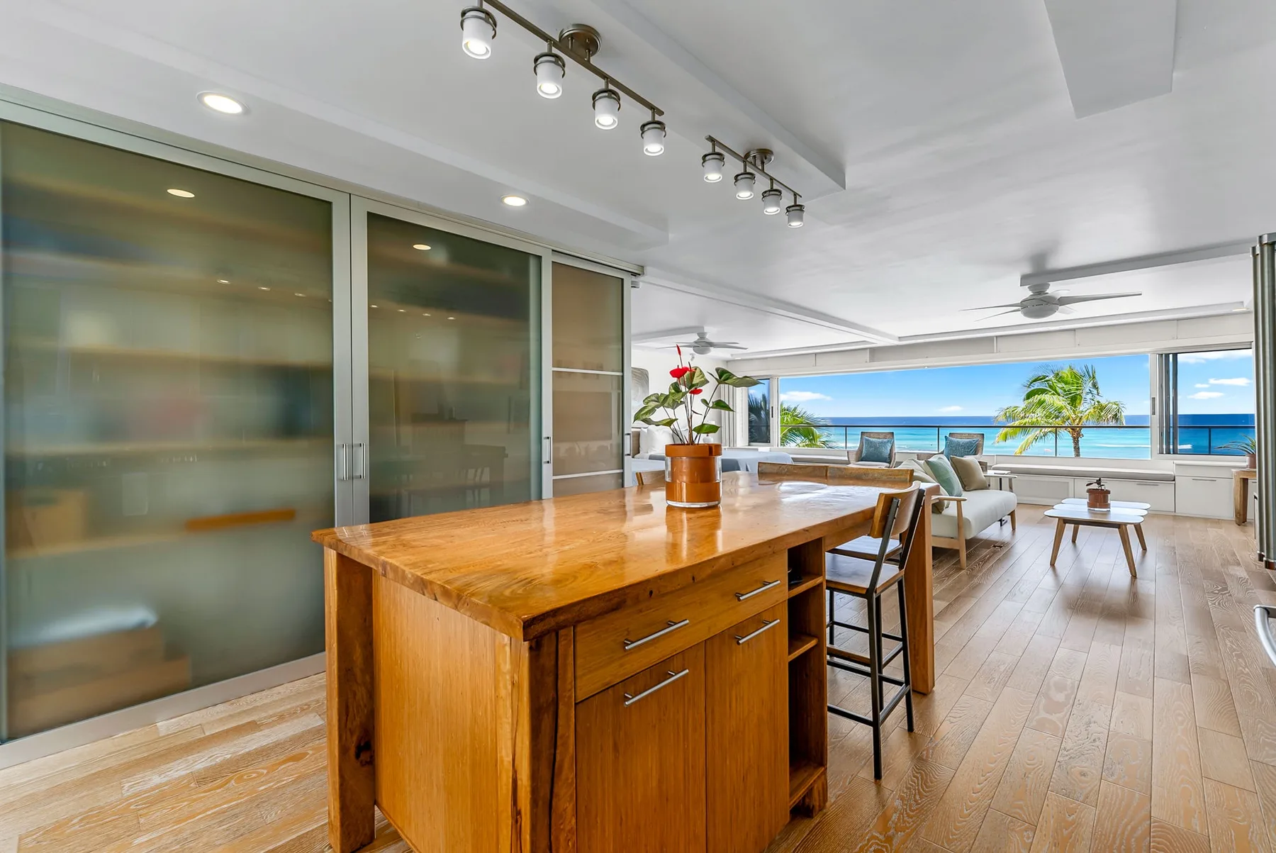 A bright open-plan living area features a wooden island and ocean views through wide windows.