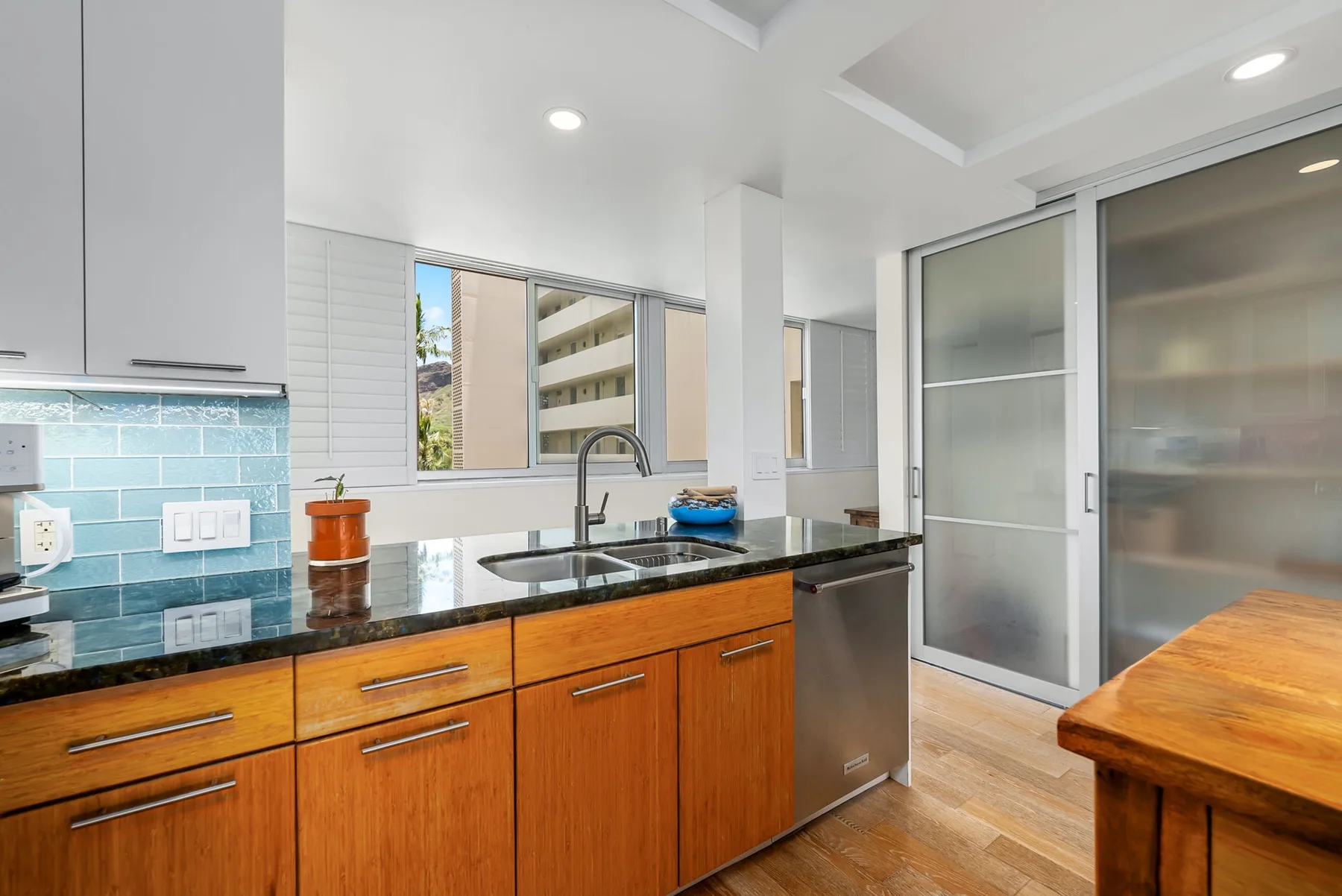 A bright kitchen with wooden cabinets, a dark countertop, and a window.
