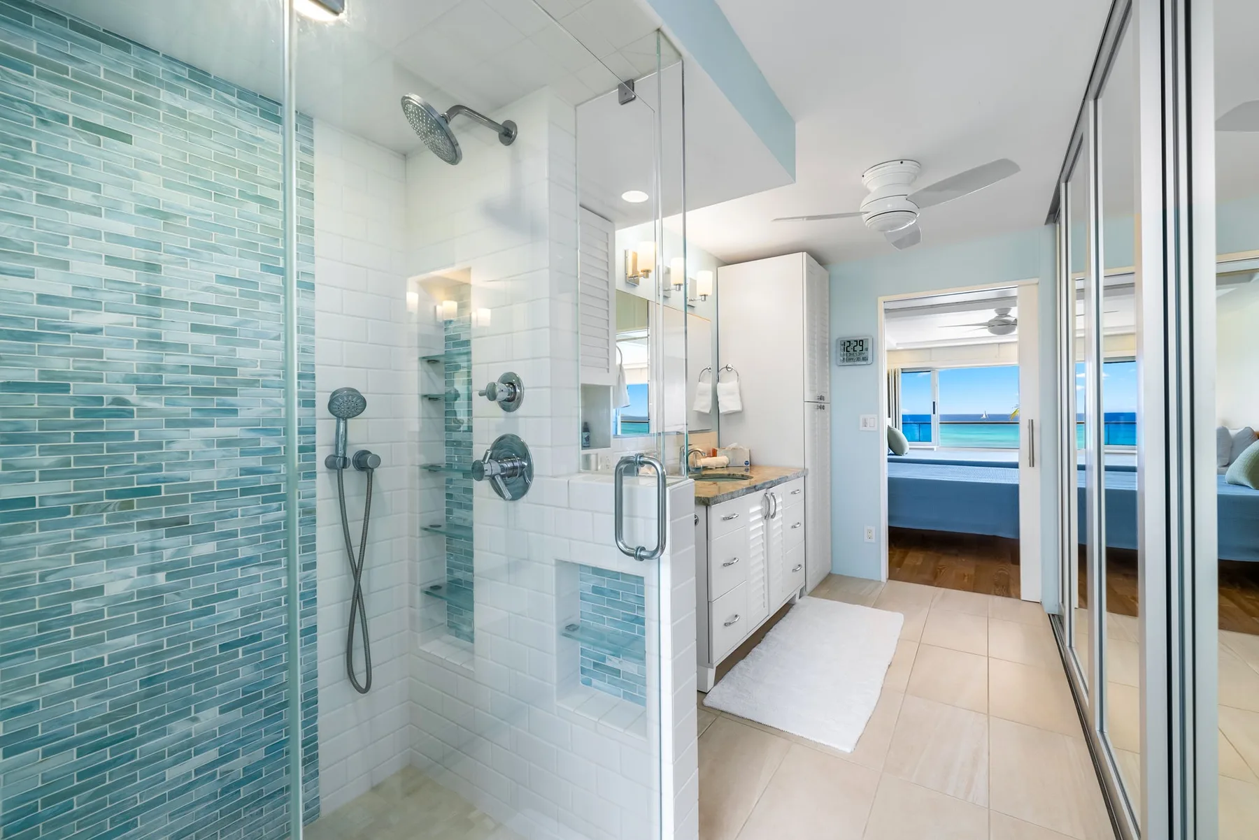 A bright bathroom with a glass shower and a vanity beside the doorway.