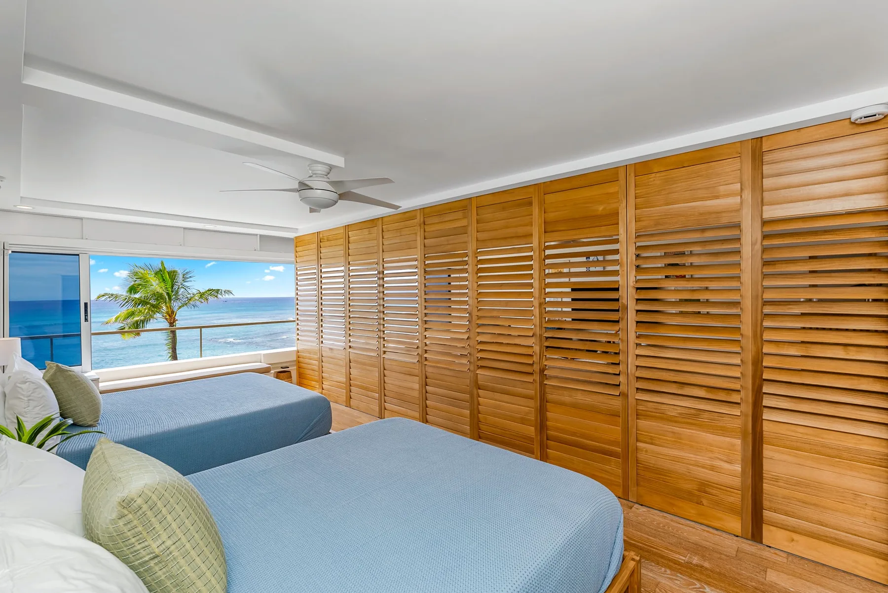 A bedroom with two beds beside a large window overlooking the ocean.
