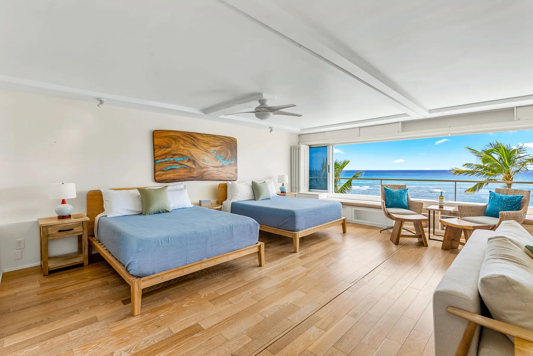 A bright bedroom with two beds and a seating area facing the ocean.