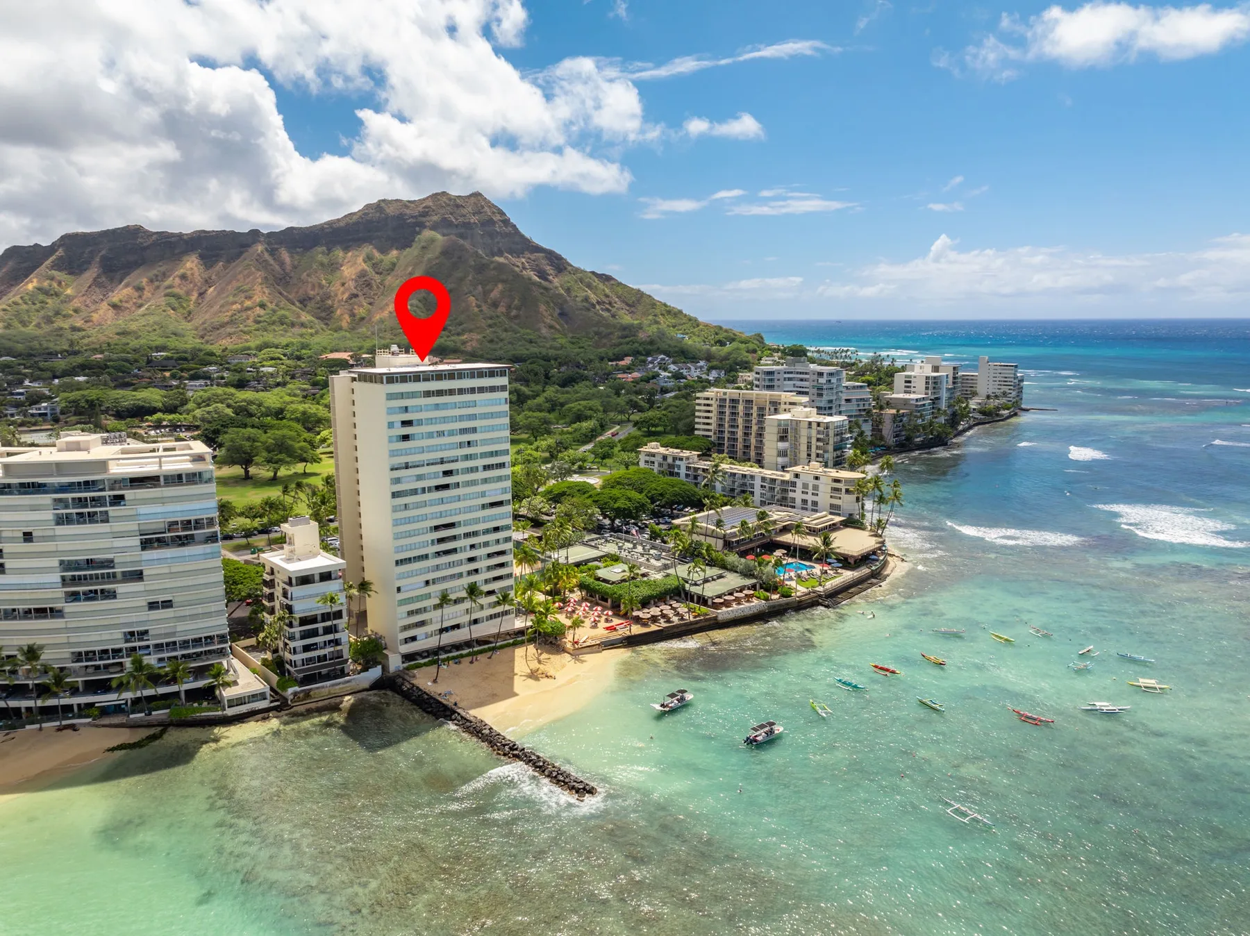 Aerial coastal cityscape with beachfront buildings, turquoise water, and a mountain behind.