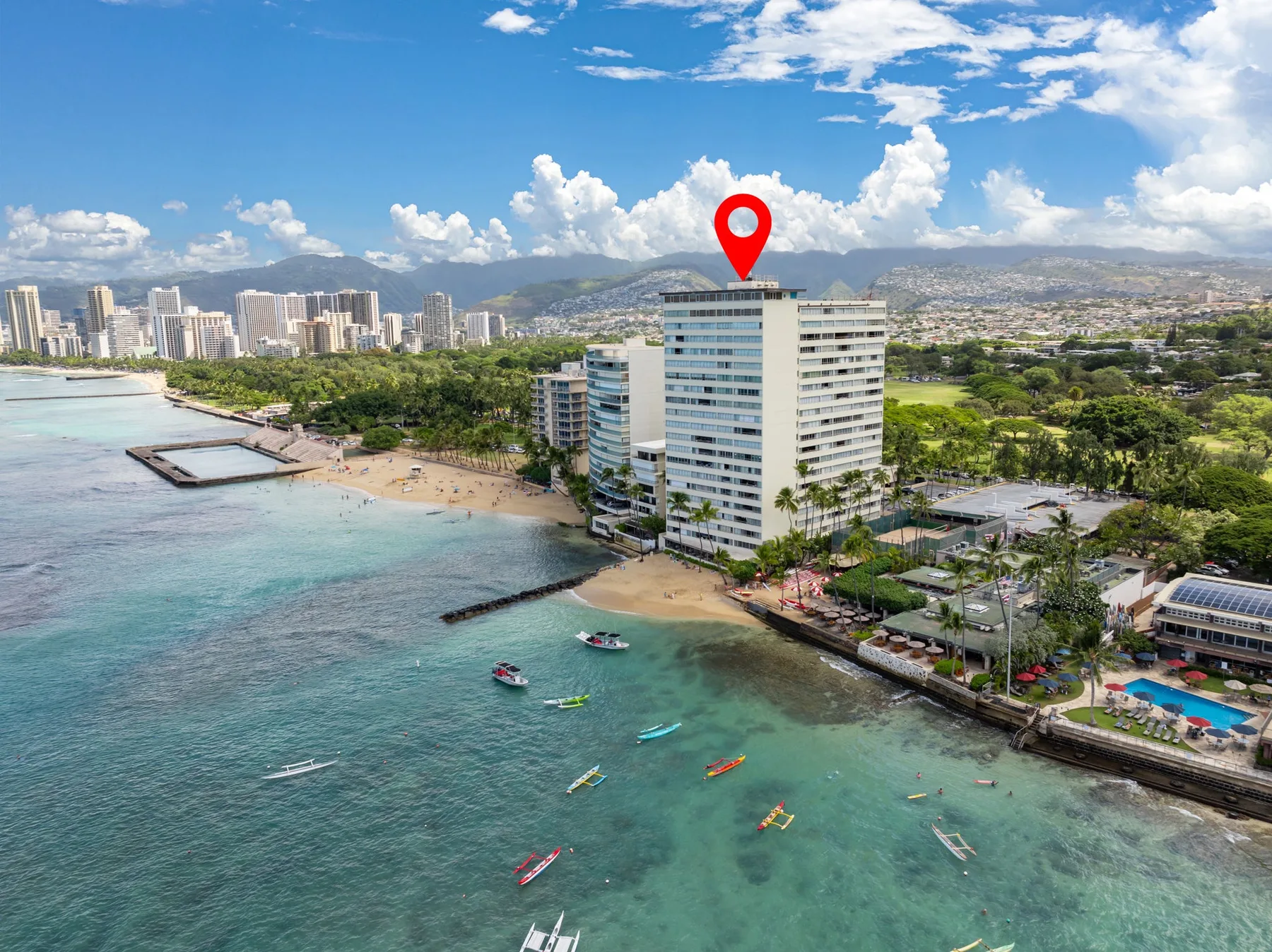 Aerial view of a waterfront city with a beach, high-rise buildings, and mountains beyond.