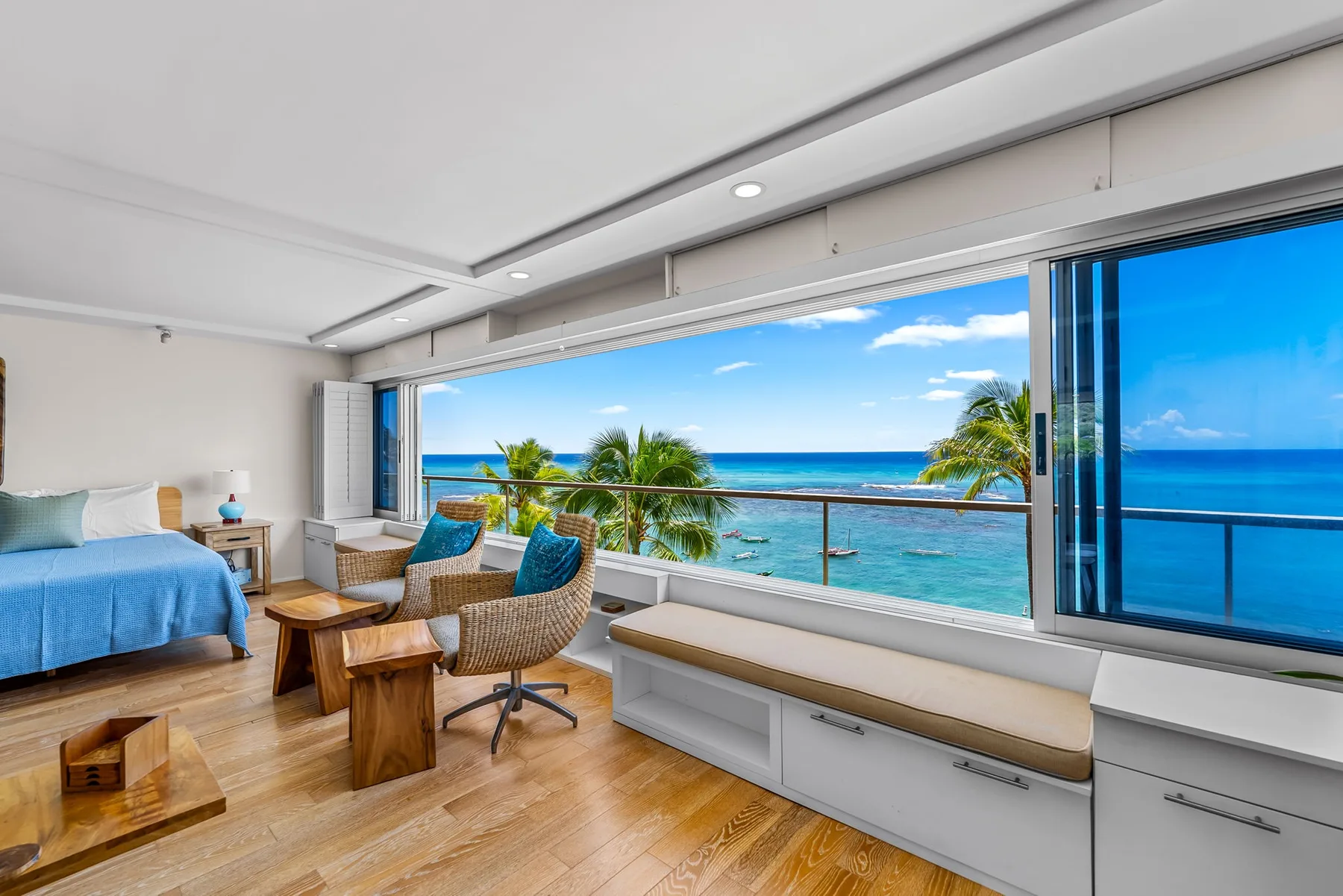 A bright bedroom with seating beside a wide window overlooking the ocean.