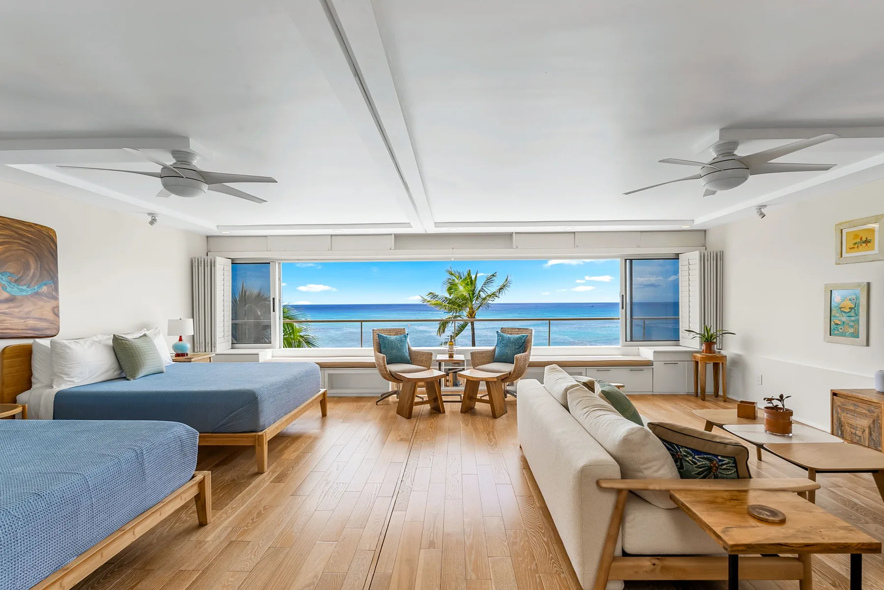 A bright living room with seating, beds, and a wide ocean view.