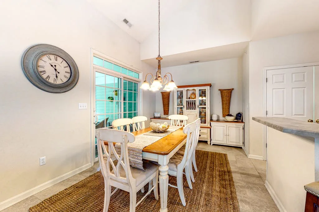 A dining area with a wooden table, white chairs, and a hanging light.