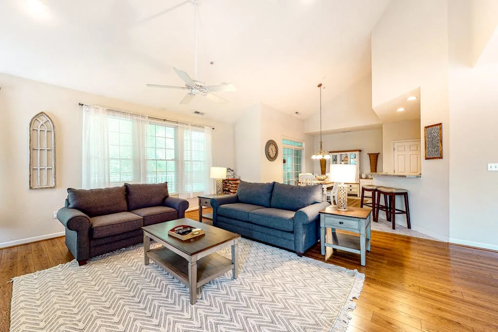 A bright living room with seating around a coffee table, opening into a dining area.