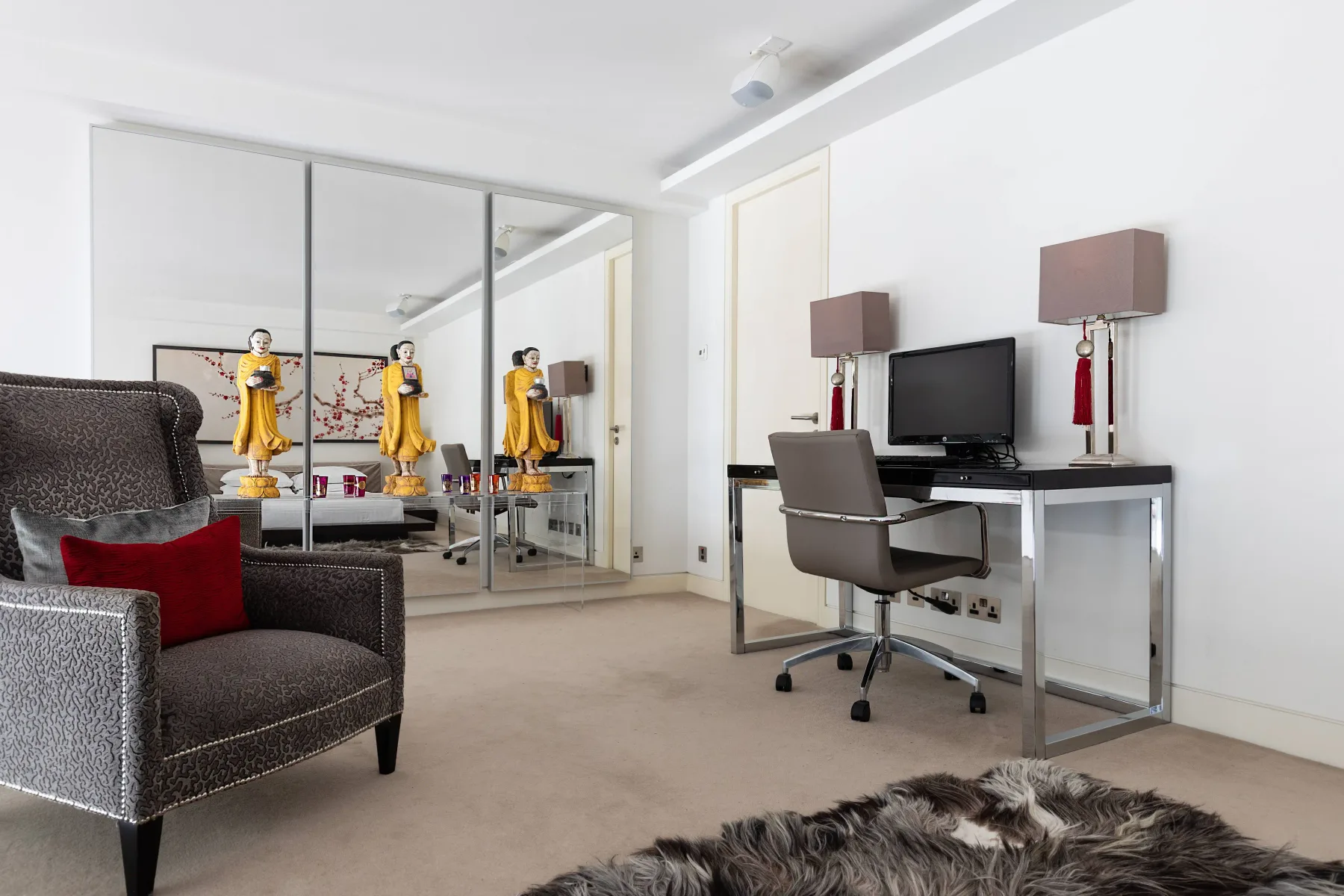 A bedroom sitting area with mirrored wardrobe doors and a desk.