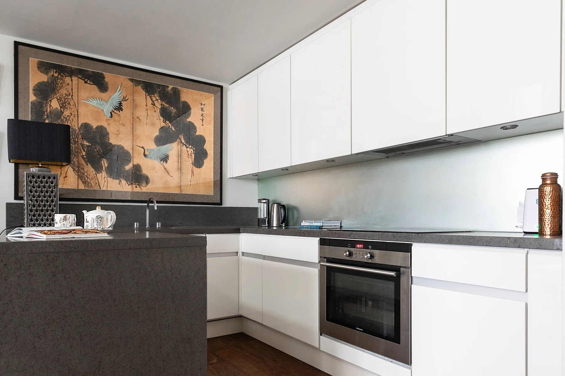 A modern kitchen with white cabinets, a dark counter, and a built-in oven.